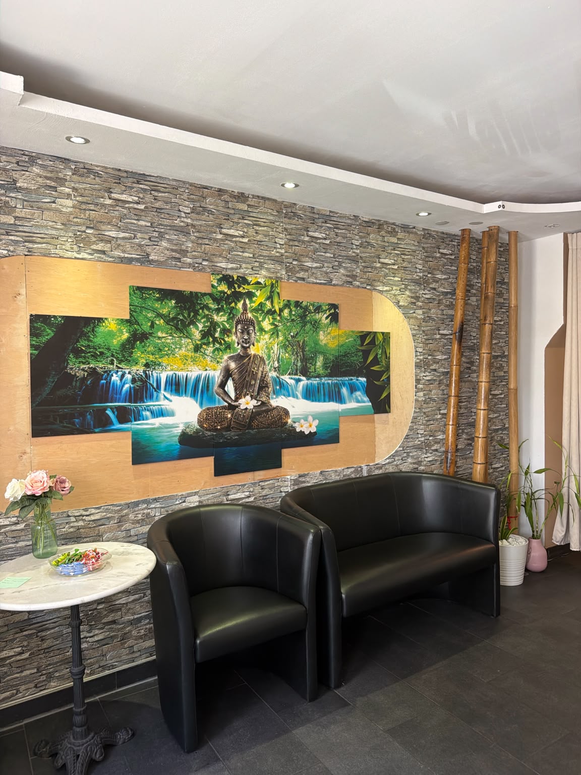 Wartebereich mit bequemen Sesseln, Buddha-Wandbild und Steinwand